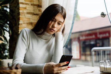 üzgün kadın bir kafede oturur ve telefonda bir ileti yazar