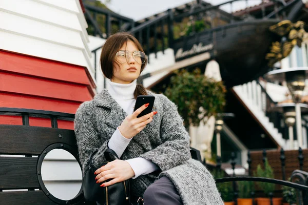 Жінка сидить на лавці в парку з телефоном в руках — стокове фото