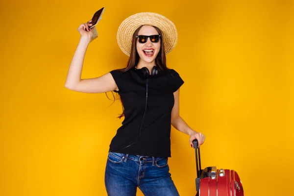 Счастливая туристическая женщина стоит рядом с красным чемоданом, и держит паспорт — стоковое фото