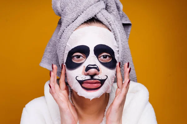 Una mujer aturdida con una toalla en la cabeza aplicar una máscara hidratante en forma de bozal de un panda — Foto de Stock