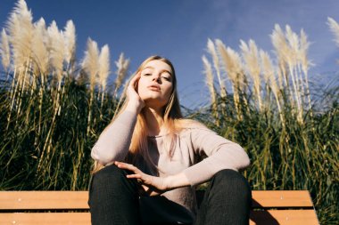 güzel kadın sazlık bir arka plan üzerinde bir bankta oturur