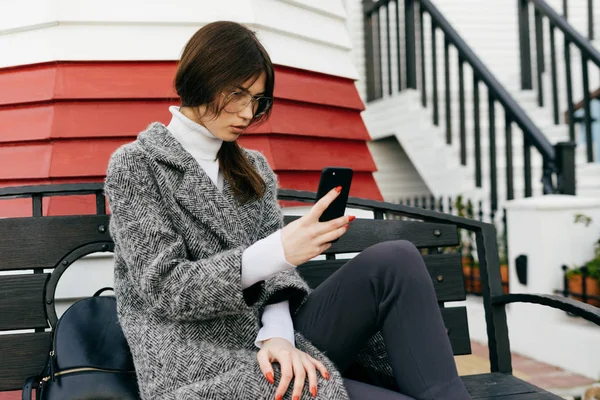 Femme à la mode s'assoit sur un banc et écrit un message au téléphone — Photo