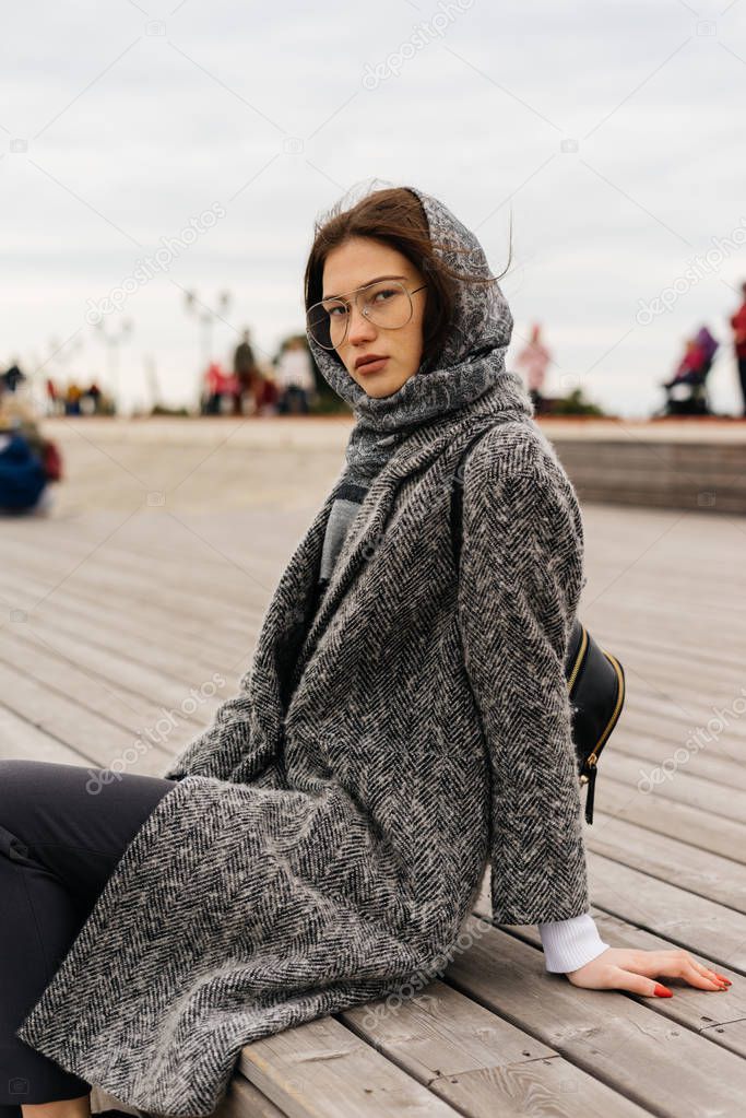 fashionable woman in glasses sits on a wooden bench
