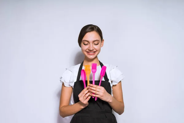 Mujer feliz en delantal sostiene utensilios de cocina en las manos — Foto de Stock