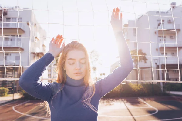 Donna pensierosa posa sullo sfondo di una griglia di pallavolo in una giornata di sole — Foto Stock