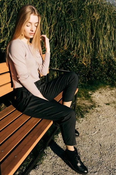 Mooie jonge blonde meisje in modieuze kleding, zittend op een bankje buiten in de zon, Streetstyle — Stockfoto