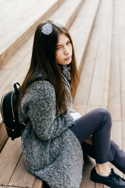 Girl in a trendy gray coat sits on the steps — Stock Photo, Image