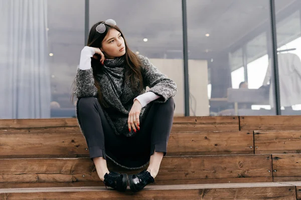 Girl in fashionable gray coat sits on steps — Stock Photo, Image