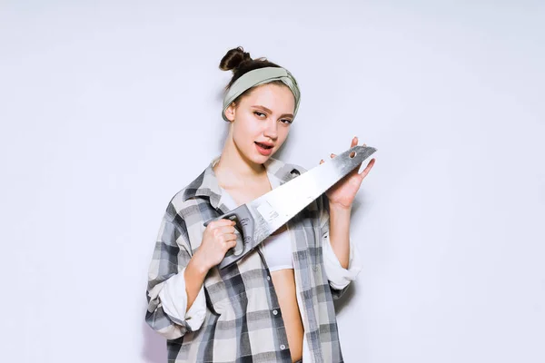 Girl in a plaid shirt holding a sharp metal saw — Stock Photo, Image