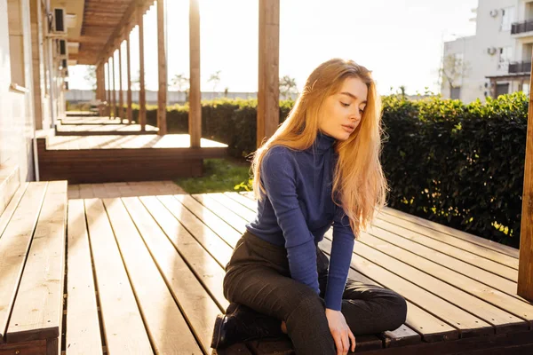 Menina em suéter senta-se ao ar livre ao sol, posando — Fotografia de Stock