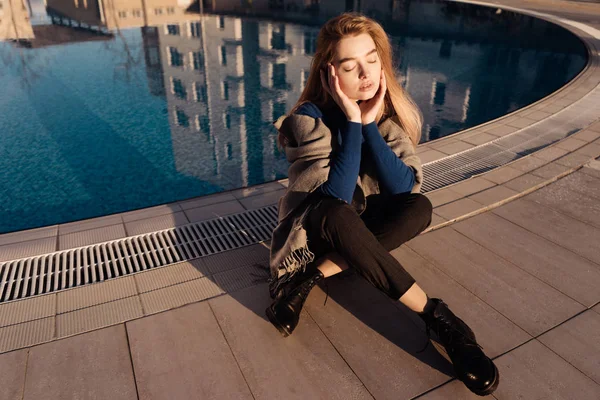 Ragazza in un maglione blu siede vicino alla piscina — Foto Stock