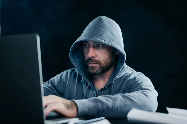 Homme pirate un ordinateur portable, dans un capot, dans le noir — Photo