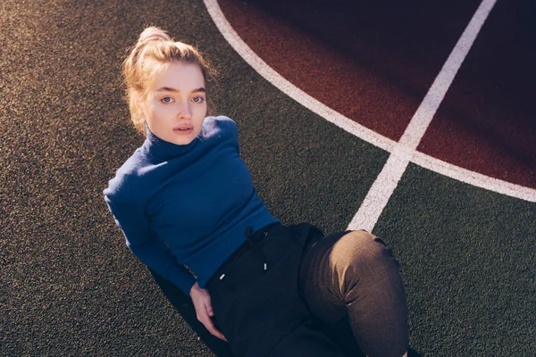 Girl in blue sweater lies on sports field — Stock Photo, Image