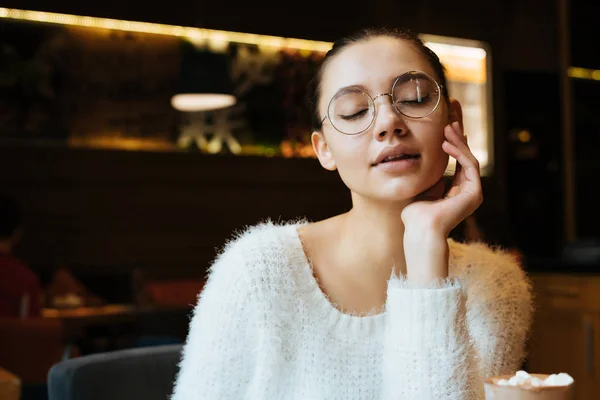 Красива молода дівчина фрілансер в окулярах, сидячи в кафе, думаючи про роботу, закрила очі — стокове фото