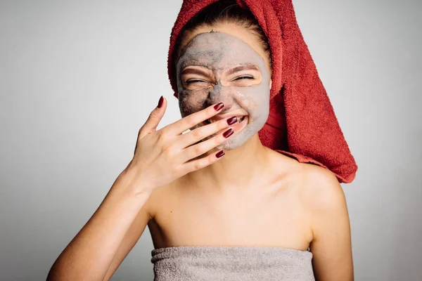 Glad skrattande flicka med en röd handduk på huvudet tillämpas en användbar mask på ansiktet — Stockfoto