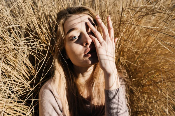 Bonito jovem loira modelo menina posando ao sol ao ar livre, cobrindo seu rosto com a mão — Fotografia de Stock