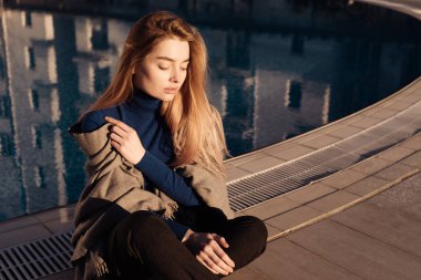 güzel genç sarışın kız mavi kazaklı güneş havuz kenarında oturur, gözler kapalı