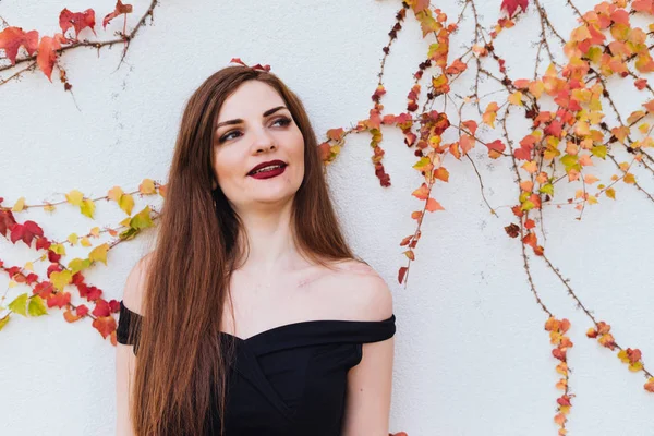 Vackra långhåriga unga kvinnan i svart klänning poserar mot vägg och leende — Stockfoto