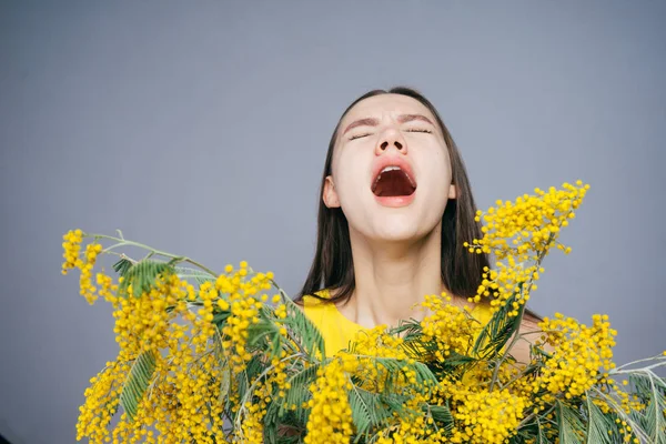 Una joven tiene un gran ramo de mimosa amarilla, estornuda porque es alérgica a las flores — Foto de Stock