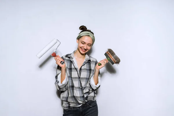 Happy young girl builder holding a brush and roller for painting walls — Stock Photo, Image