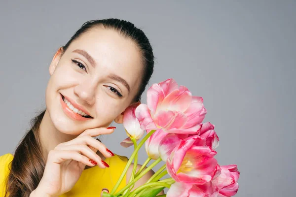 Schöne junge Mädchen in einem gelben Kleid lächelt, hält einen Strauß duftender Frühlingsblumen — Stockfoto