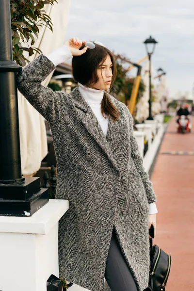 Fille confiante aux cheveux foncés en manteau gris à la mode marchant à l'extérieur, style de rue — Photo