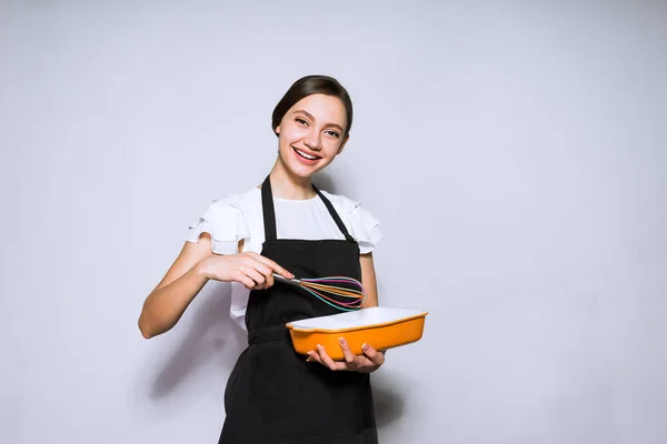 Щаслива молода дівчина готує в чорному фартусі, готуючи смачний торт, посміхаючись — стокове фото