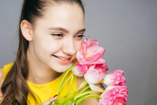 Beautiful happy young woman in yellow dress rejoices in spring and smiles holding a bouquet of pink flowers — Stock Photo, Image