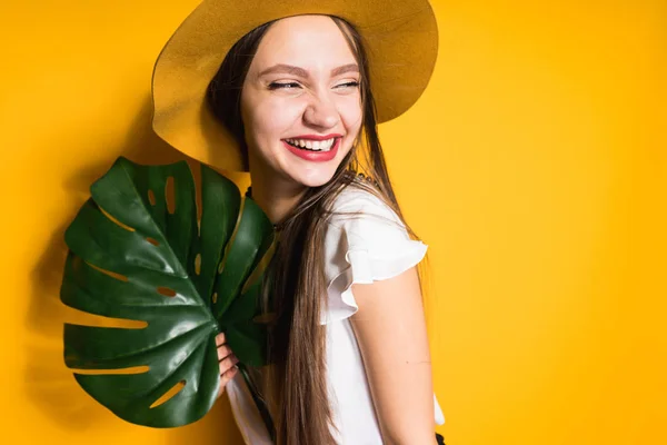 Szczęśliwa dziewczyna długowłosy model w modny kapelusz, śmiejąc się i pozowanie, przytrzymując zielony liść — Zdjęcie stockowe