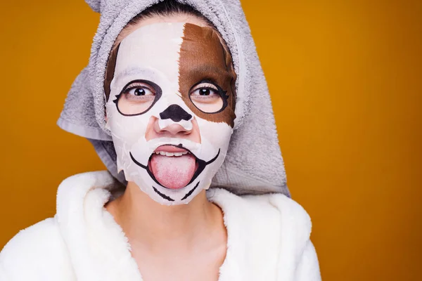 Grappig meisje met een handdoek op haar hoofd tong, waarop gezichtsmasker met een foto van de snuit van een hond — Stockfoto
