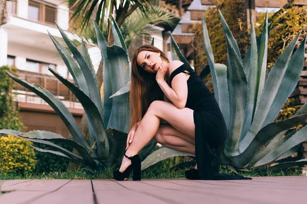 Sexy luxuriöse junge Frau in einem schwarzen Kleid, die durch den Garten geht und ein reiches Leben und Freizeit genießt — Stockfoto