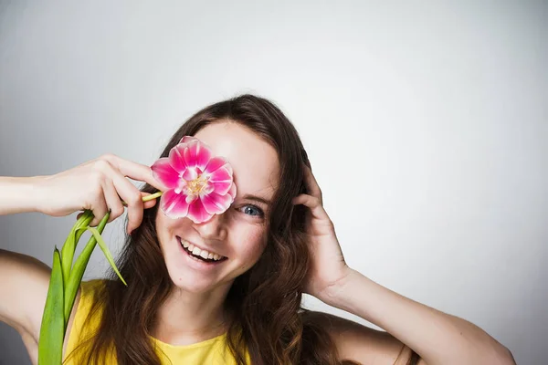 Feliz joven de ojos azules chica sosteniendo flor rosa, sonriente, buen humor — Foto de Stock