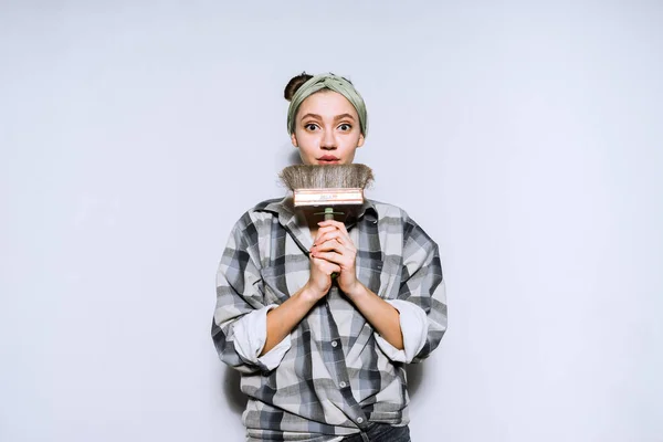 Cute young girl in a plaid shirt holding a paintbrush for painting the walls, doing repairs in her new apartment — Stock Photo, Image