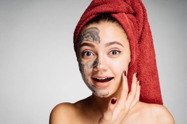 güzel genç kız başında kırmızı bir havlu ile yararlı kil maskesi yüzünde uygular.