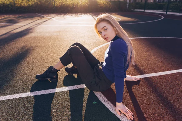 Elegante jovem loira modelo menina em camisola azul senta-se no parque infantil e posando — Fotografia de Stock