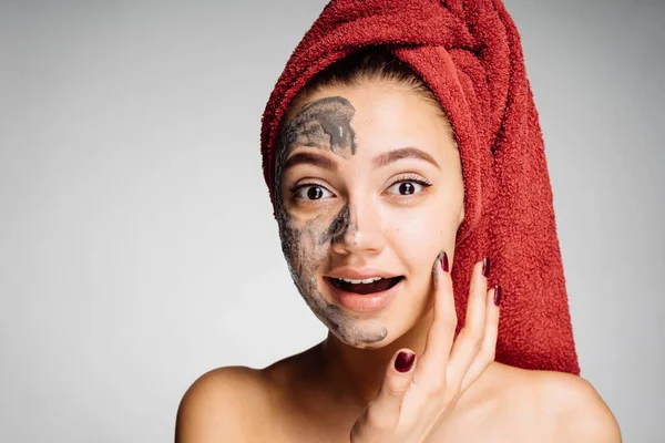 güzel genç kız başında kırmızı bir havlu ile yararlı kil maskesi yüzünde uygular.