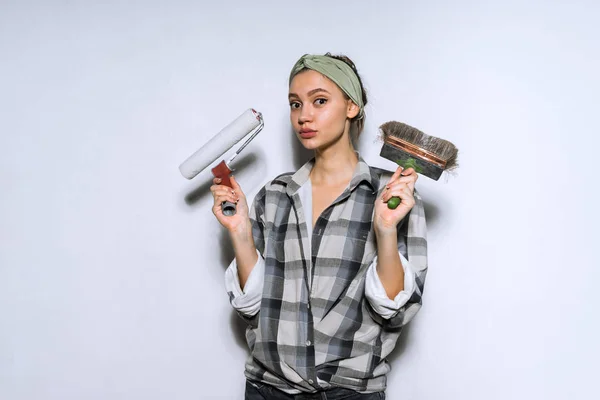 Young girl in plaid shirt holding brush and roller for painting walls — Stock Photo, Image