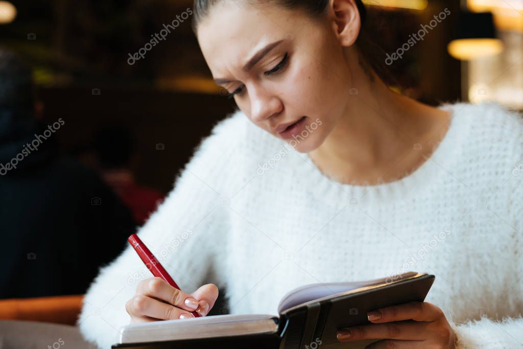 young girl freelancer sits in a cafe, writes in a notebook, concentrates
