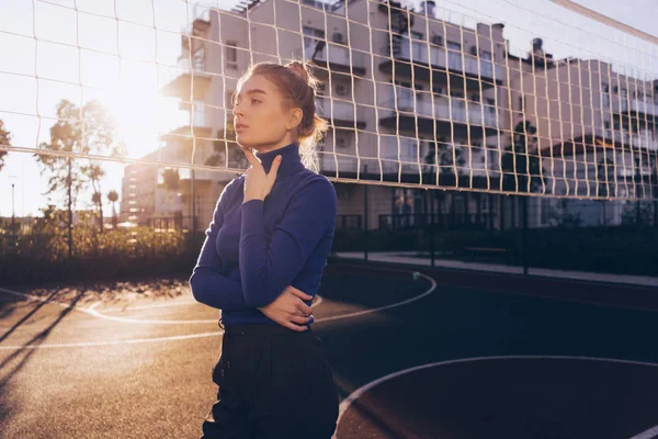 Mooi stijlvol meisje blond model in een blauwe trui poseren op een sportveld in de zon — Stockfoto