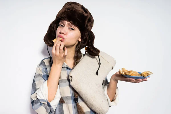 Genç Rus kız siyah kürk şapka içinde karnaval kutluyor, lezzetli sıcak krep yiyor — Stok fotoğraf