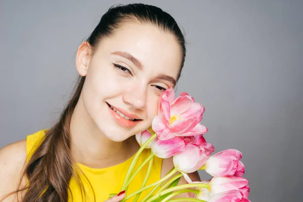 पीले पोशाक में खुश युवा लड़की मुस्कुराती है, सुगंधित गुलाबी फूलों और मुस्कुराहटों का गुच्छा रखती है — स्टॉक फ़ोटो, इमेज
