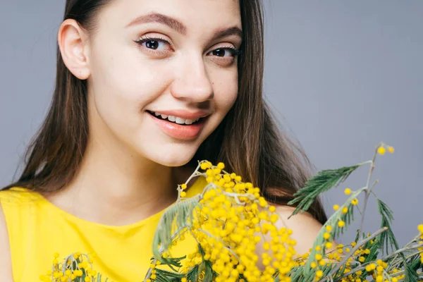 Heureuse jeune fille en robe jaune sourit, tient jaune mimosa parfumé — Photo