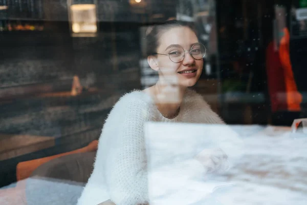 Милий молода дівчина студент в окулярах сидить в кафе після уроків і посміхається — стокове фото