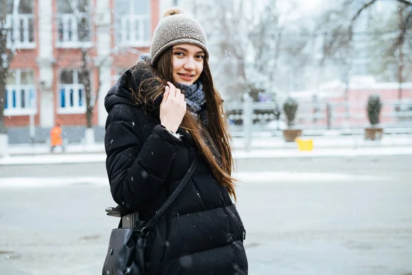 Молодая длинноволосая девушка в теплой куртке гуляет по улицам города в зимнюю погоду — стоковое фото