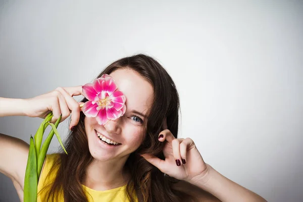 Niña en vestido amarillo sonriendo, sosteniendo flor rosa — Foto de Stock