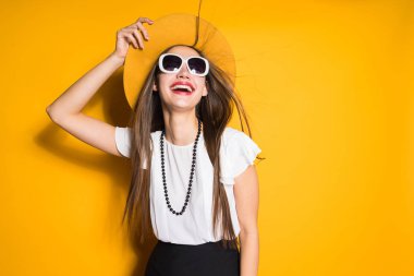 mutlu genç kız şapka ve gülüyor ve Sarı zemin üzerine poz güneş gözlüğü