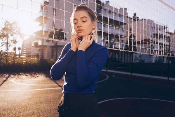 Stylisches junges Mädchen im blauen Pullover posiert auf einem Sportplatz in den Strahlen der Morgensonne — Stockfoto