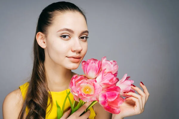 Attractive female in yellow dress holds a bouquet of fragrant pink flowers and smiles — Stock Photo, Image