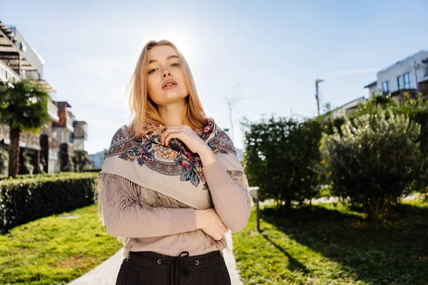 Bela jovem loira com um lenço em seus ombros andando pelas ruas da cidade, posando nos raios do sol da primavera — Fotografia de Stock