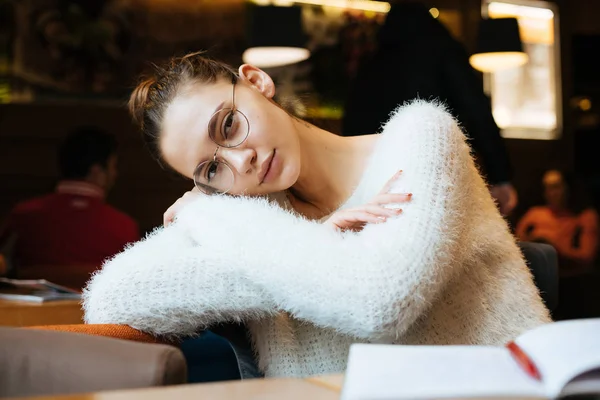 Lindo joven estudiante en una chaqueta blanca y gafas sentado en un café después de la escuela — Foto de Stock